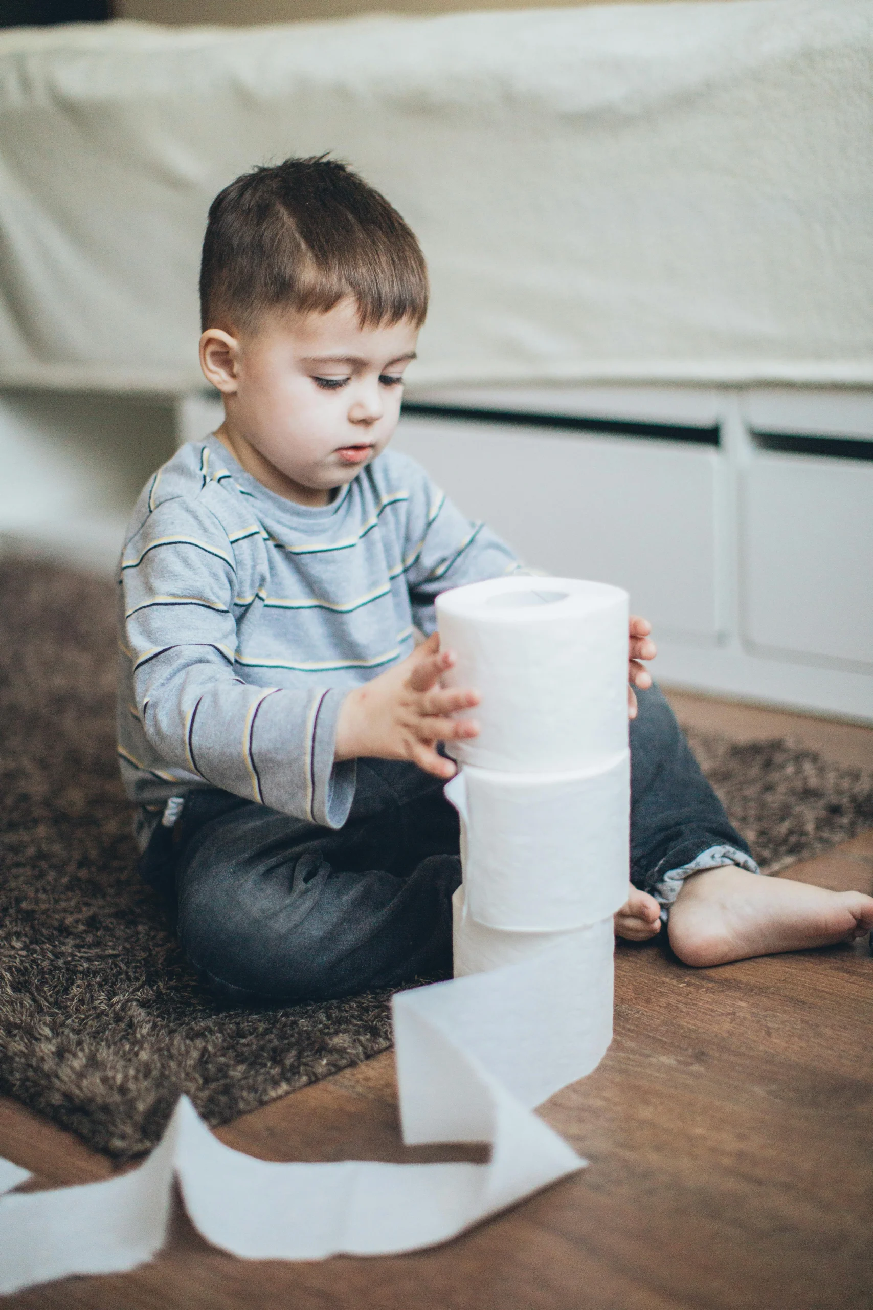 Adorable child stacking toilet paper rolls playfully indoors.
