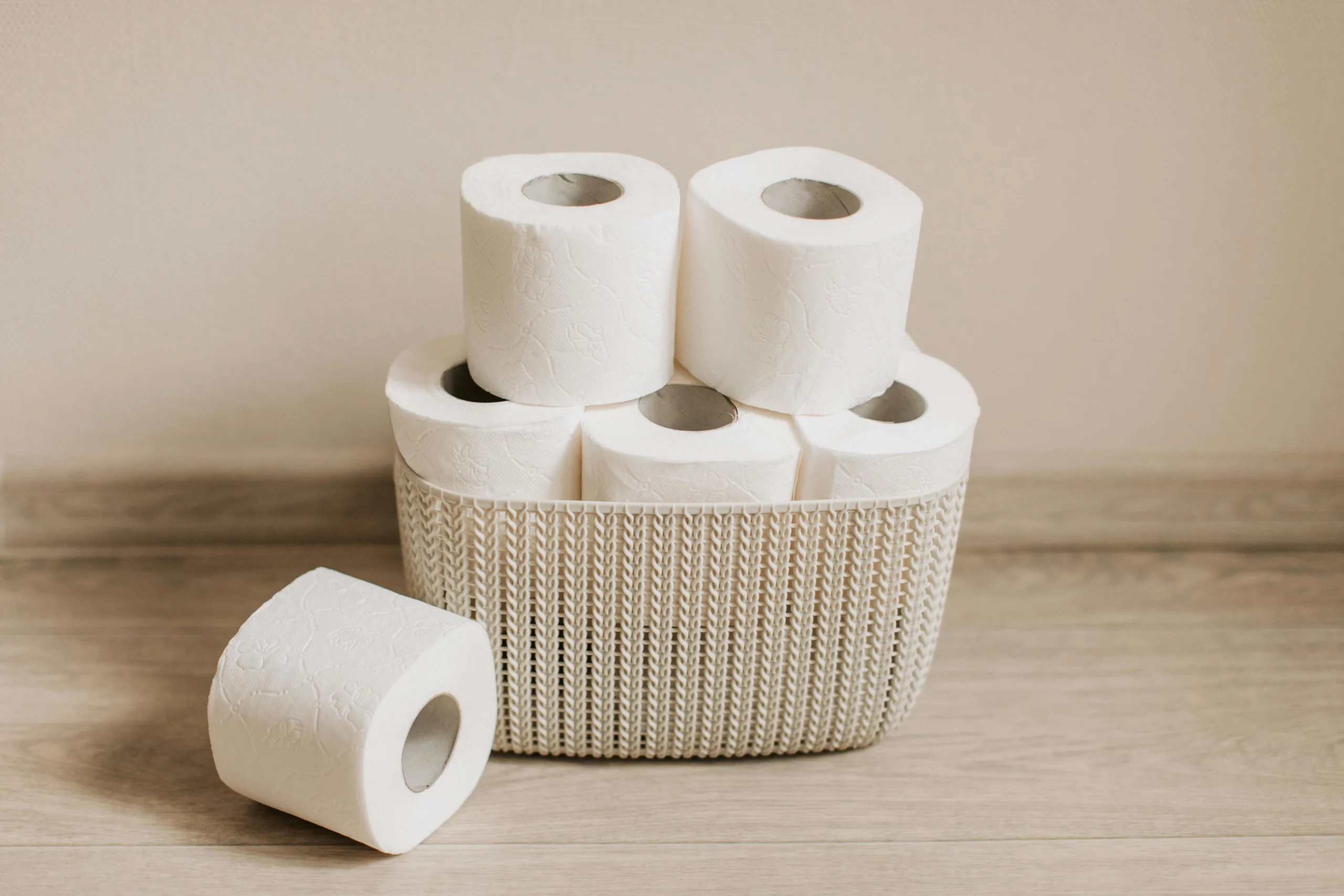 Basket of white toilet paper rolls neatly arranged on a wooden floor.