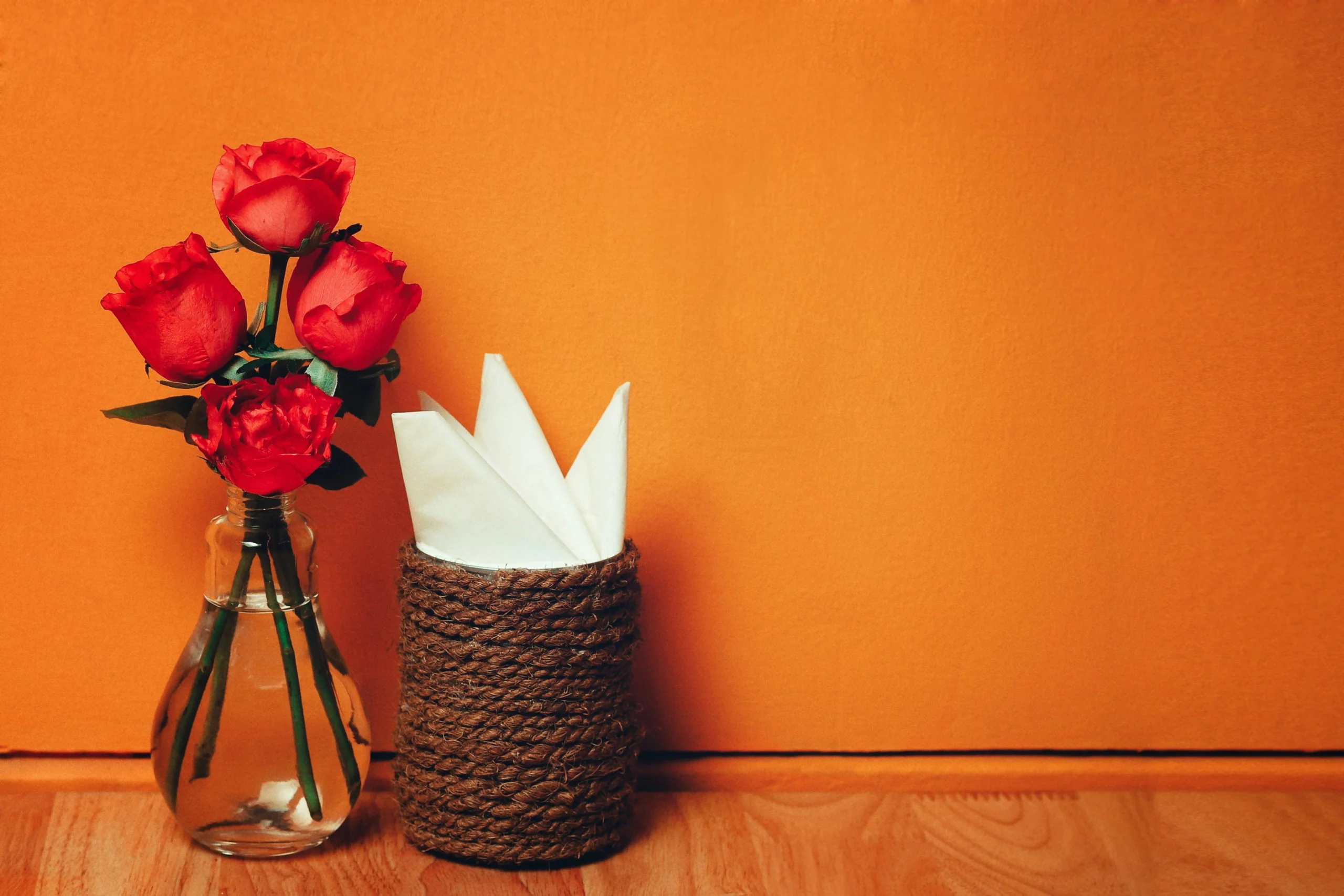 Charming arrangement of red roses in a vase with napkins, set against an orange background.