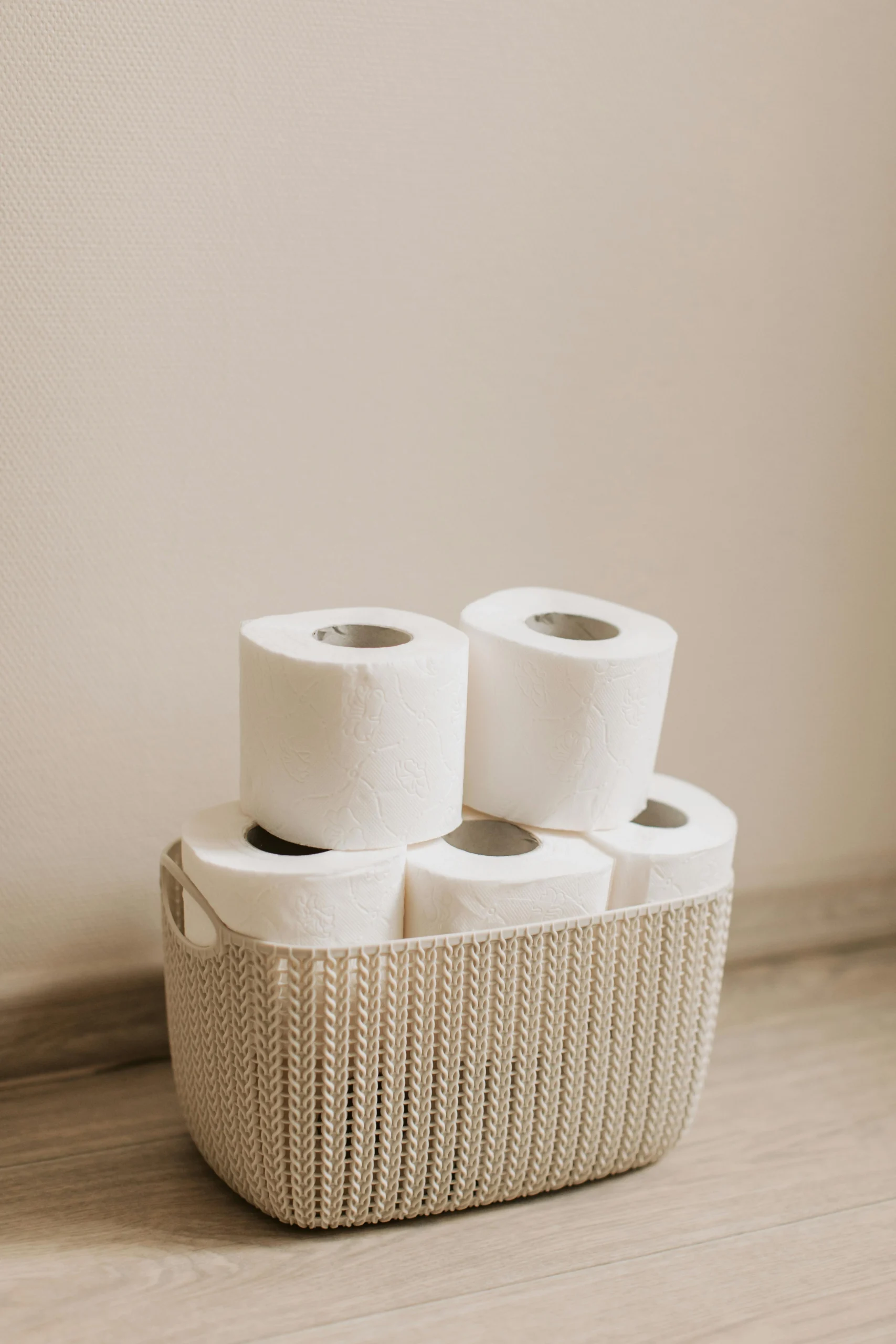 Minimalist photo of toilet paper rolls in a woven basket on a wooden floor.