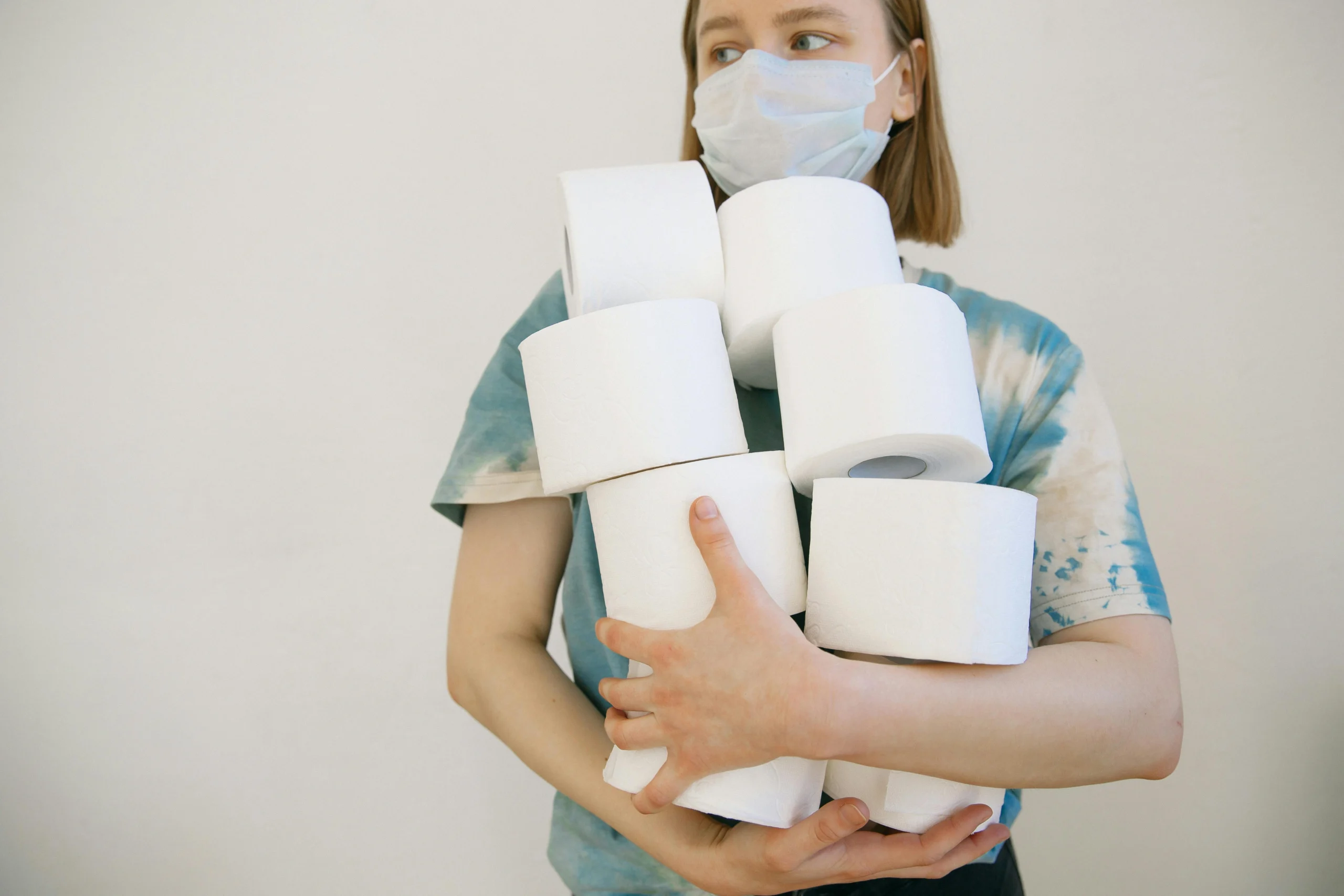 Woman wearing a face mask holding several toilet paper rolls indoors.