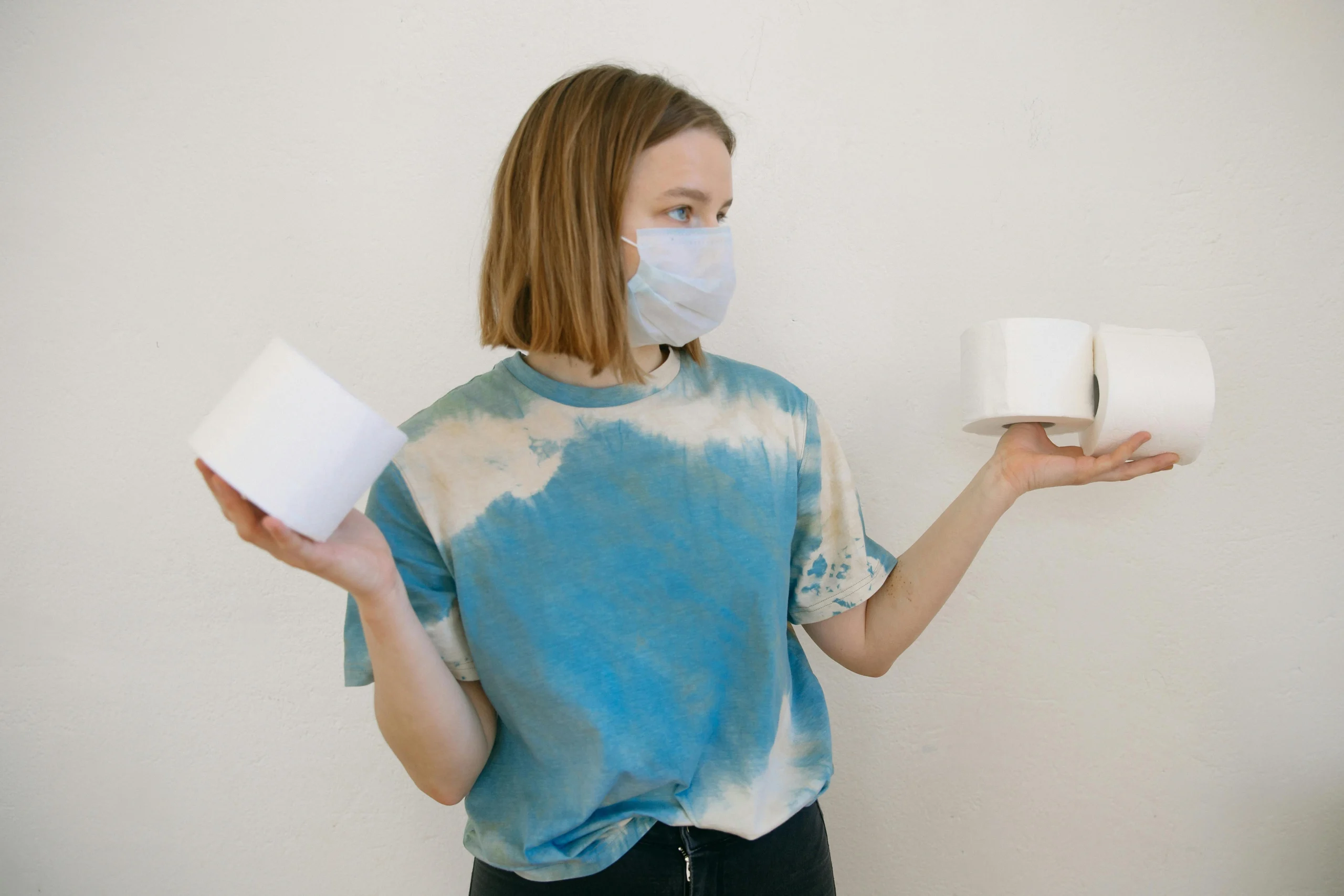 Woman with face mask holding toilet paper rolls indoors during pandemic.