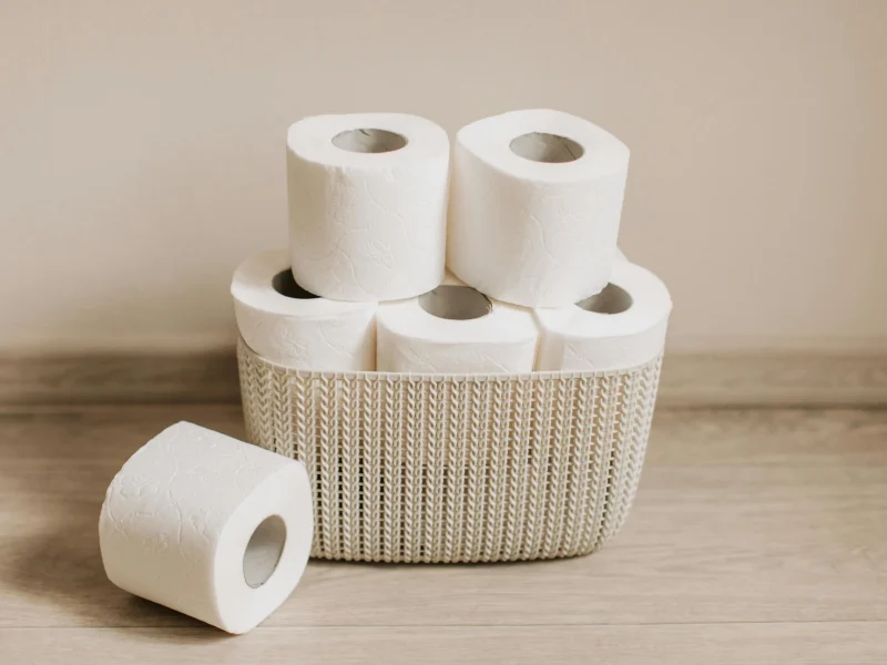 Basket of white toilet paper rolls neatly arranged on a wooden floor.