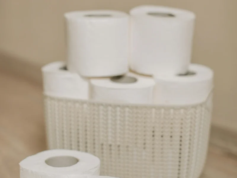 Collection of toilet paper rolls neatly arranged in a woven basket on a wooden floor, indicating hygiene and cleanliness.